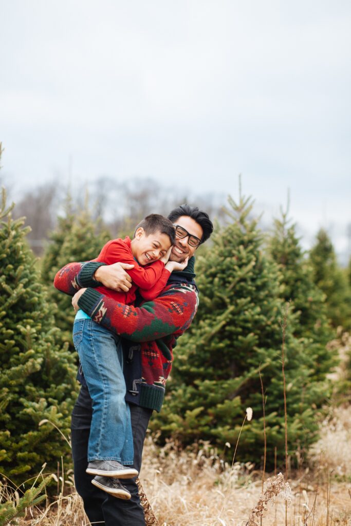 HappyChildHuggingDadInAChristmasTreeFarm